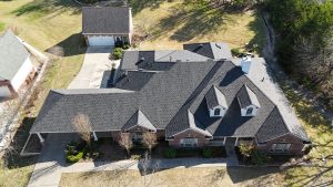 Aerial top-down view of a large residential house showing a complex roof structure with multiple slopes, ridges, dormers, and attached garage.